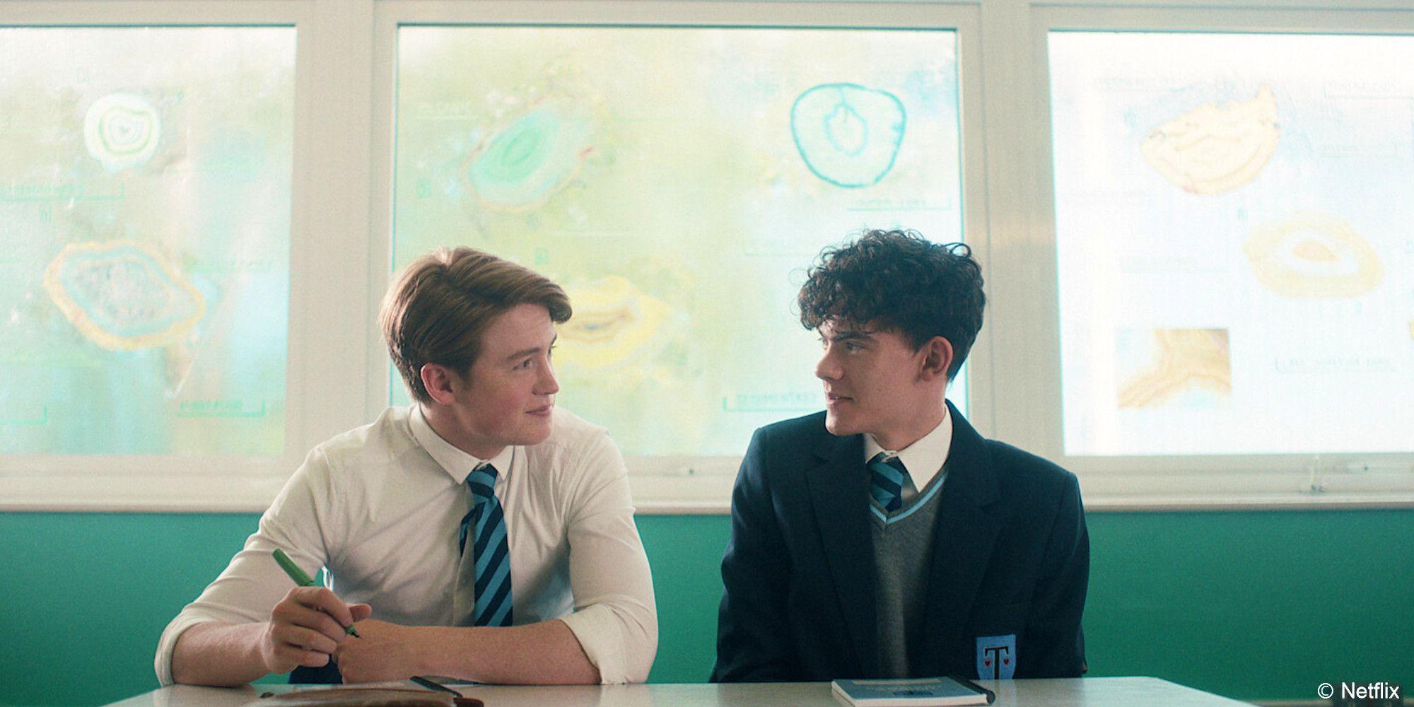 Heartstopper Charlie and Nick look sweetly at one another while sitting side by side in a classroom 